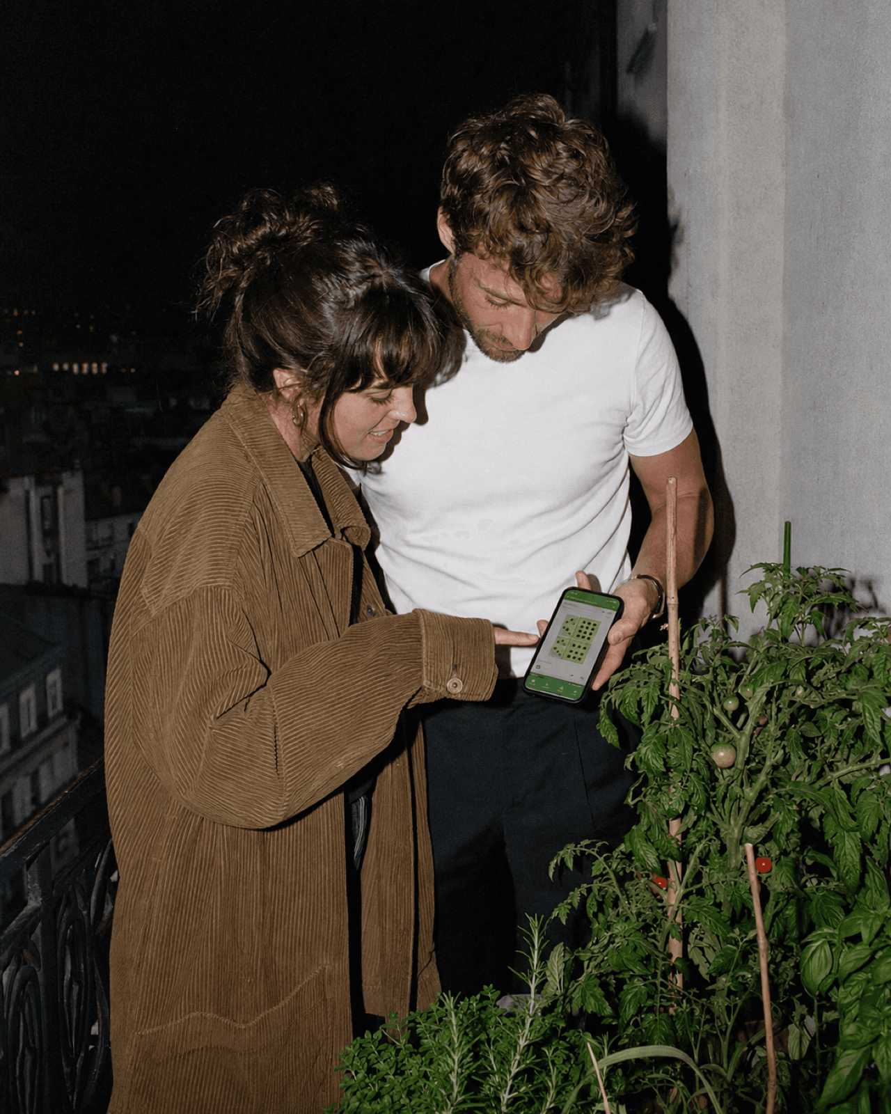 Couple sur un balcon parisien consultant l'app Irrigate le soir