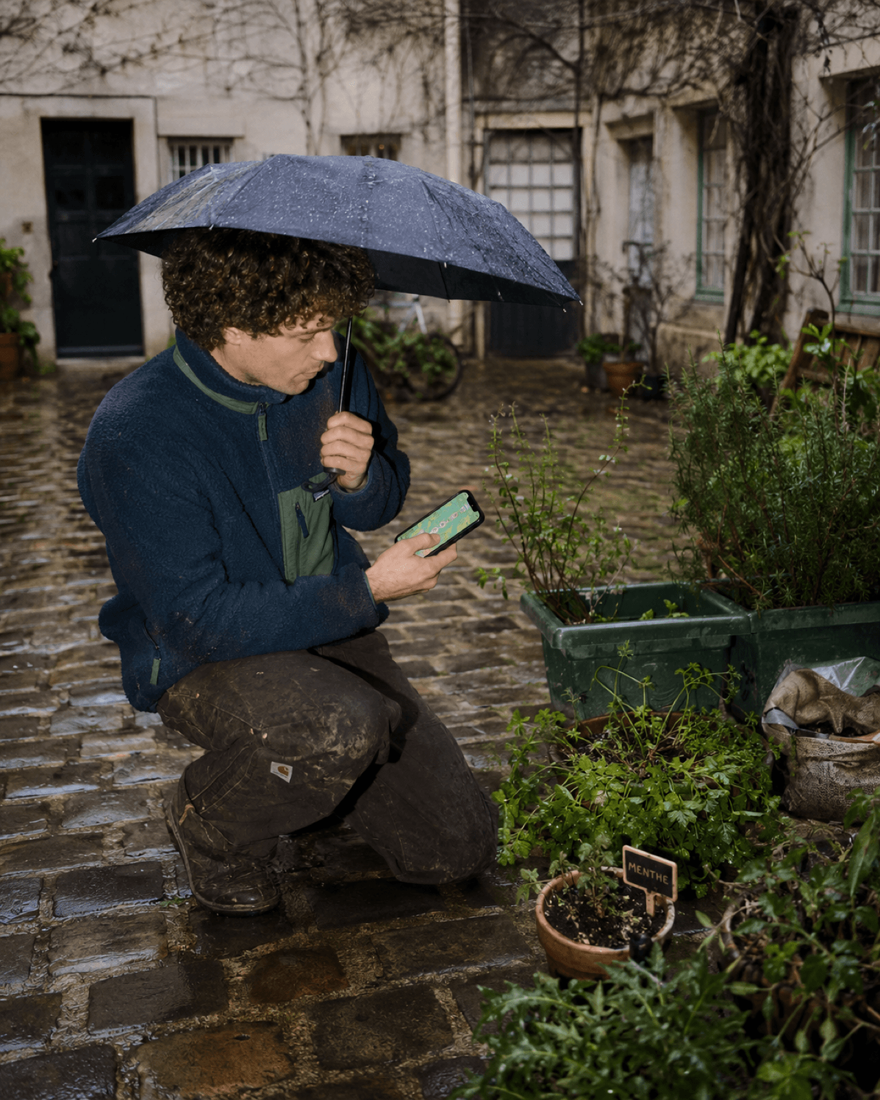 Jardinier vérifiant l'arrosage sous la pluie dans une cour pavée